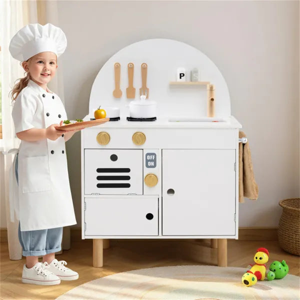 Child in chef's outfit standing next to a toy kitchen set in a room.