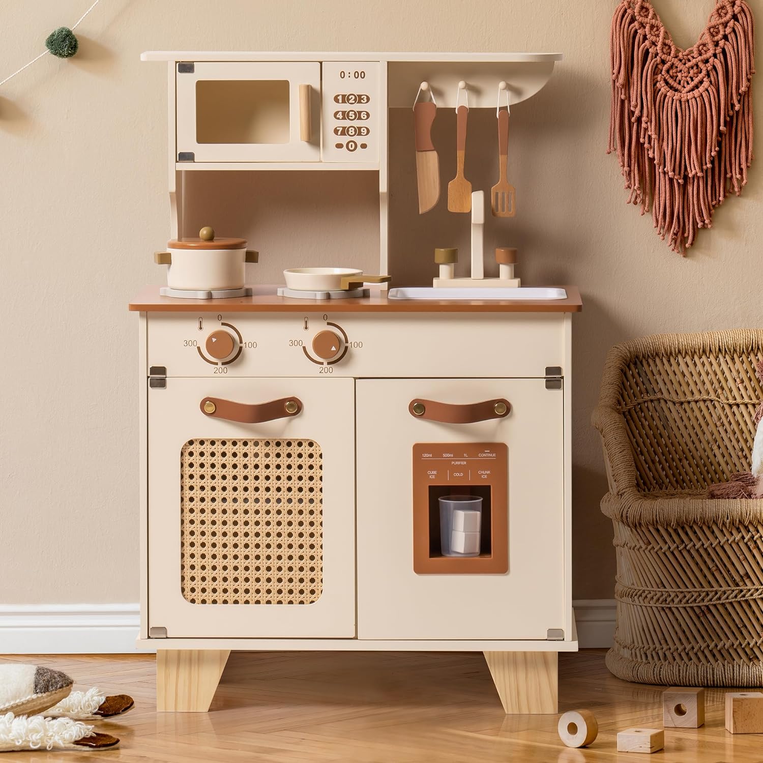 Children's play kitchen set with wooden cabinets and accessories on a beige wall background.
