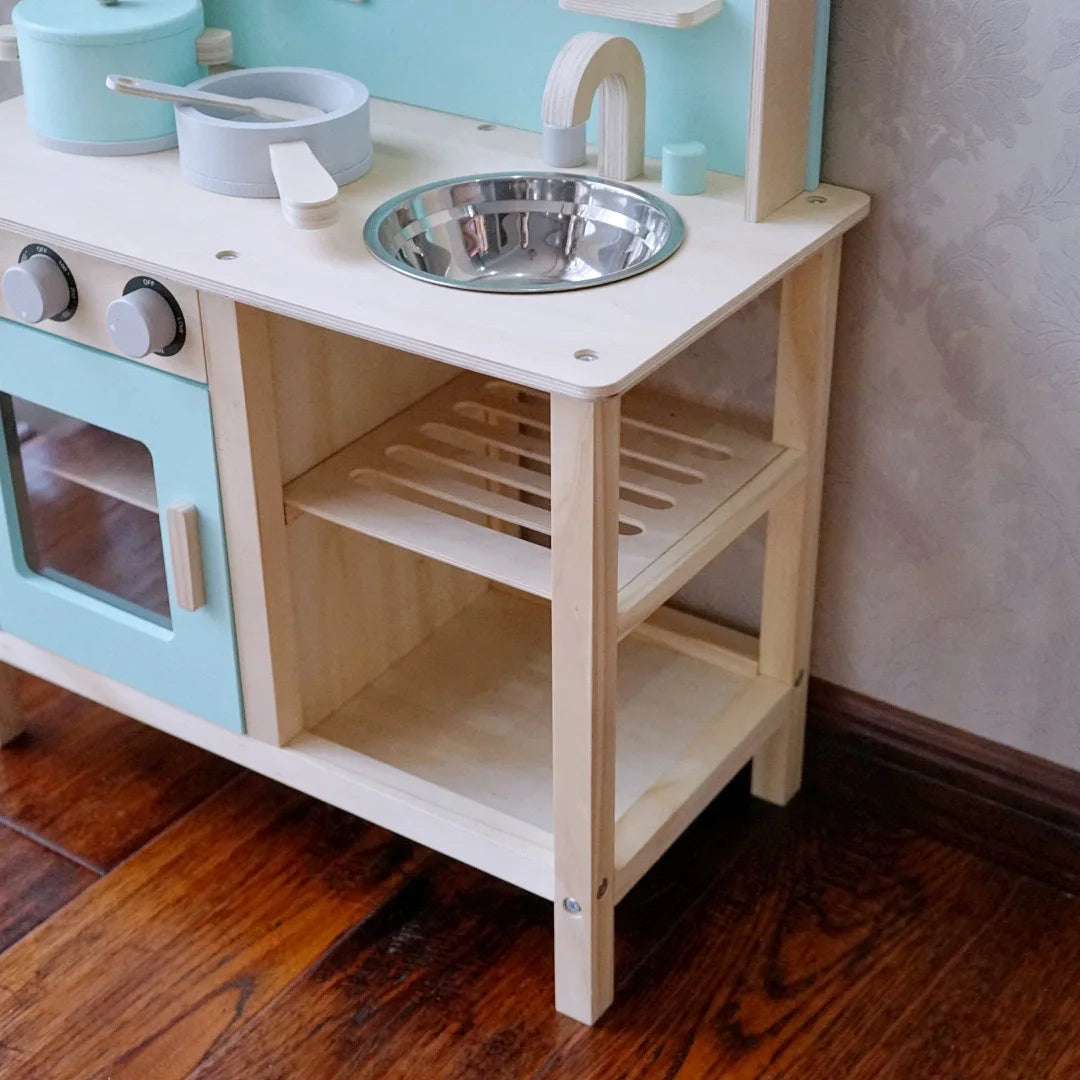 Children's wooden play kitchen set with toy stove, sink, and utensils on a wooden floor.